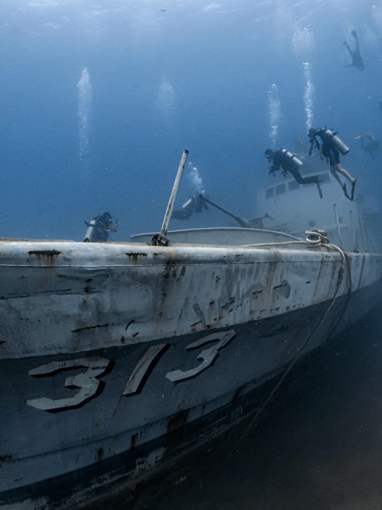 HTMS Sattakut (313) shipwreck resting on the ocean floor near Koh Tao, covered in coral and surrounded by marine life.