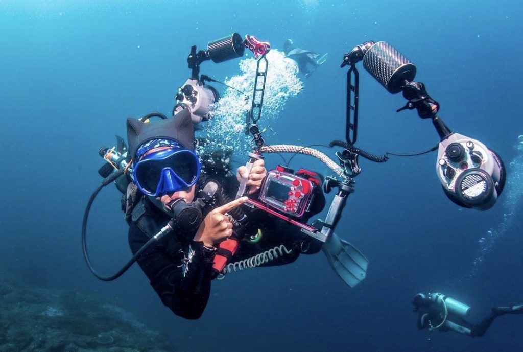 Diver underwater with a camera, capturing photos of marine life and coral reefs in the clear waters of Koh Tao