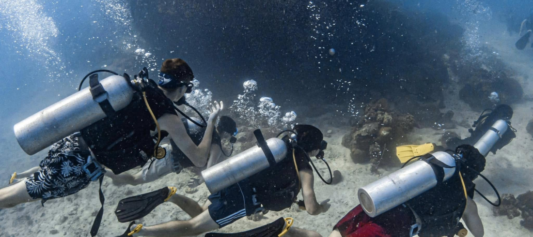 Three scuba divers exploring vibrant coral reefs and marine life in the crystal-clear waters of Koh Tao, showcasing the thrill of underwater adventures.